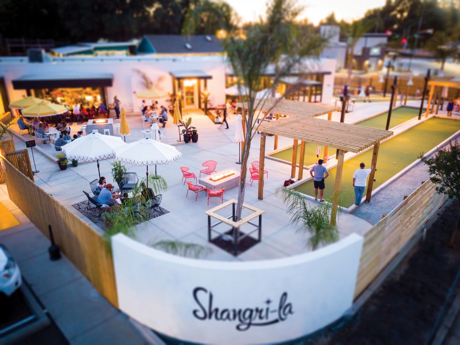 The 6,000-square-foot patio at Shangri-la evokes a Palm Springs resort vibe with two bocce courts, three firepits, towering palm trees, tables shaded by fringed yellow umbrellas, and an open-air bar. (Photo by Jeremy Sykes)