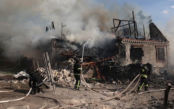 Smoke billows from a burnt-out house while rescue workers hose it with water