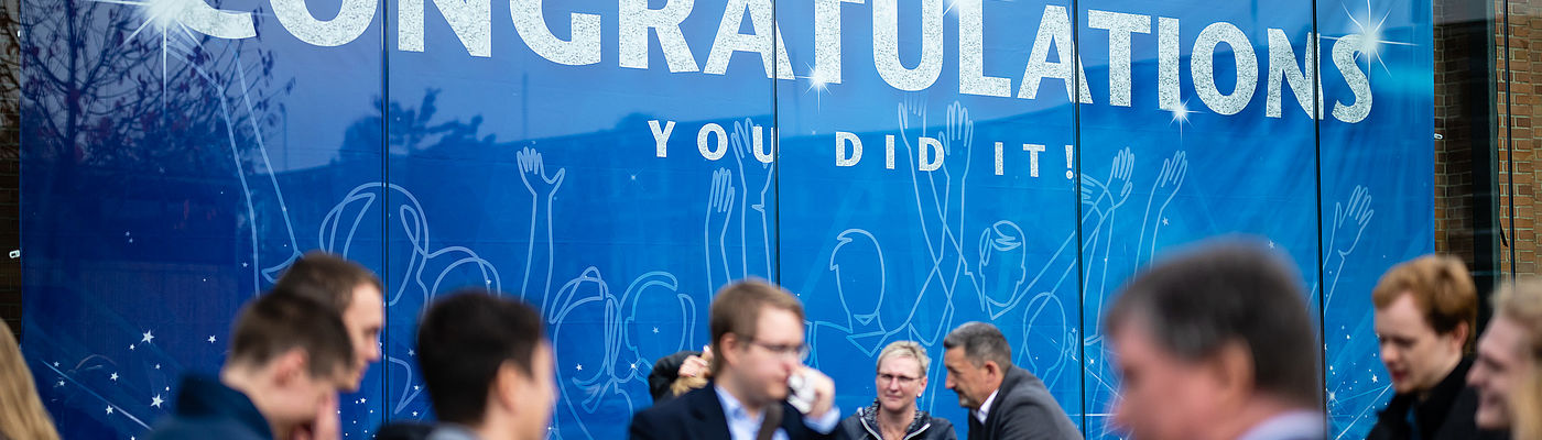 Absolventinnen und Absolventen vor dem Banner in Halle 17 bei der Verabschiedung 2022