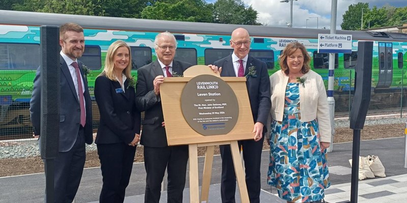 First Minister John Swinney, Transport Secretary Fiona Hyslop and project partners pose for a photo with the new plaque at Leven Station. A specially wrapped train is in the background