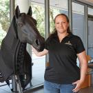 A model of a horse and a woman in blue UC Davis shirt stand in front of a window