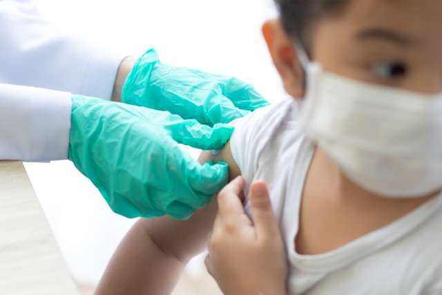 Pediatric doctor holds performing vaccination on child. 