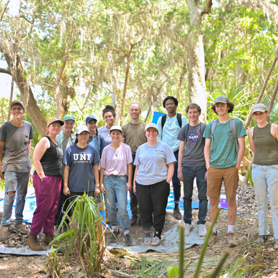 Group of students standing and smiling in a group, in the forest, surrounded by green trees