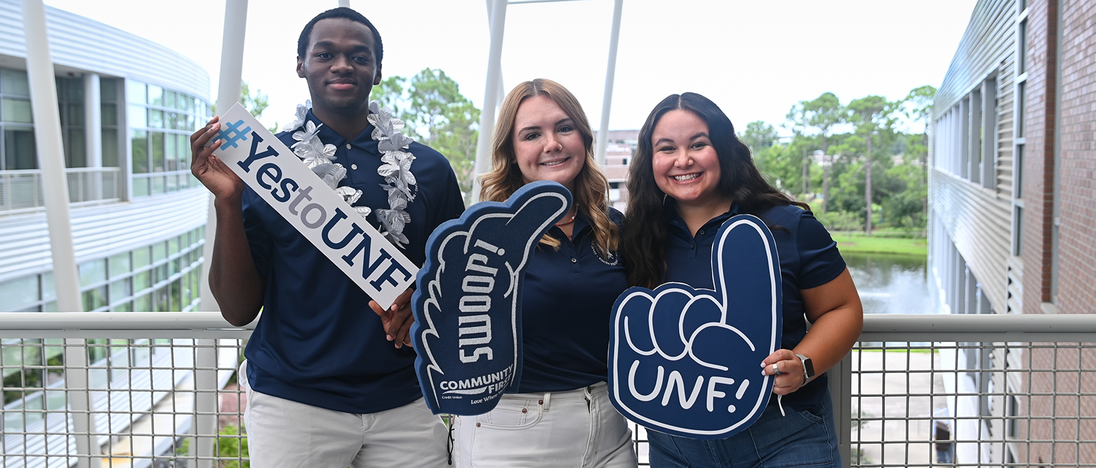 three students holding signs saying #yestounf swoop unf