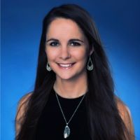 Headshot of Andrea Hartley with black shirt and necklace with blue background