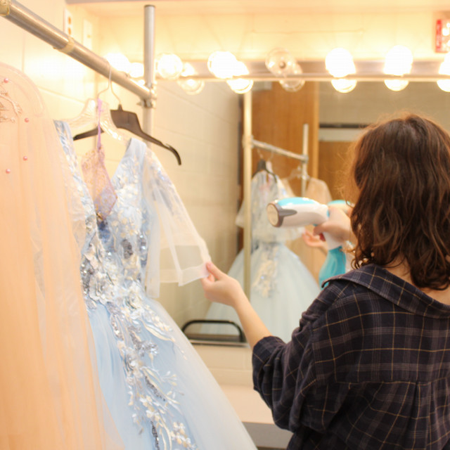 A student steams a blue costume dress. 