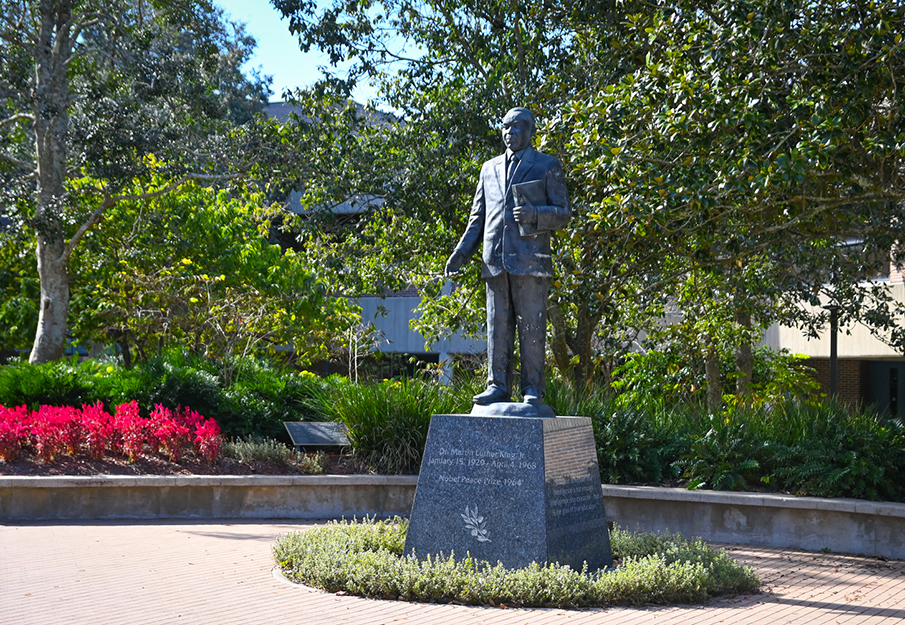 MLK statue in Peace Plaza on a sunny day with red flowers in the background