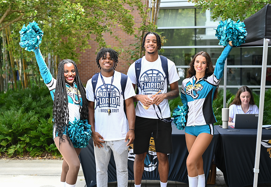 Two UNF students standing next to two Jacksonville Jaguars cheerleaders near the Jaguars season ticket sale booth