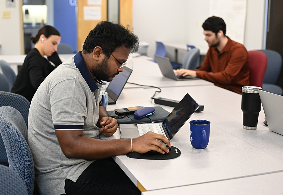 Three graduate computing students working on their laptops in a study room