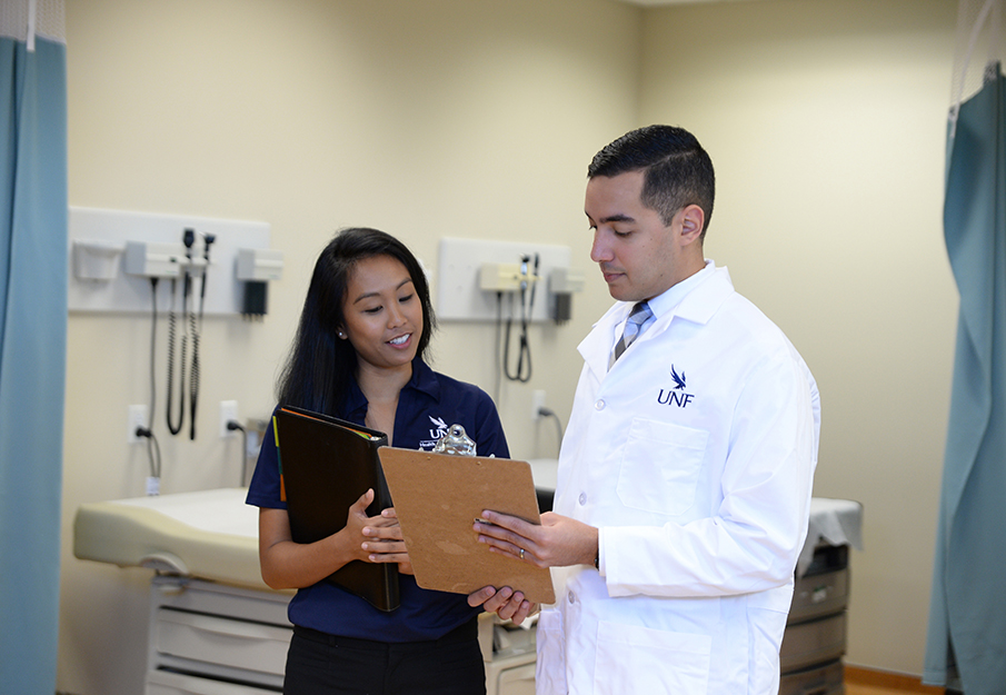 Two UNF students looking at a clipboard, one wearing a white coat