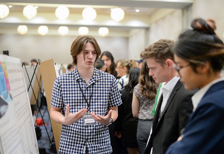 Student standing at poster board discussing his research with other students