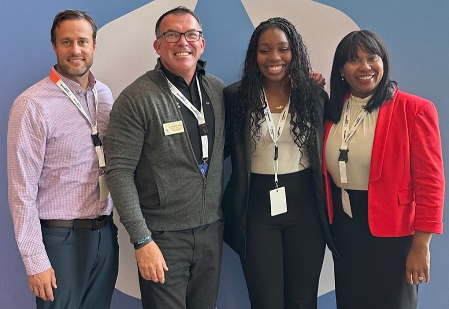 Joshua Covey, Matthew Ohlson, Alum Mercedes Sapp and Dr. Monica Moore posing in front of a FranklinCovey sign