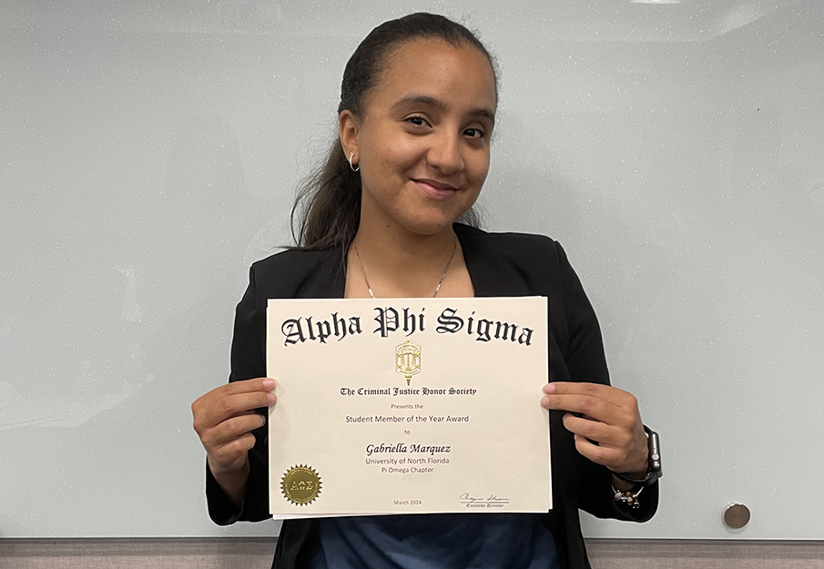 Gabriella Marquez holding up an Alpha Phi Sigma Student Member of the Year Award certificate