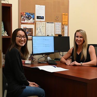 Advisor and student smiling for a photo at a desk