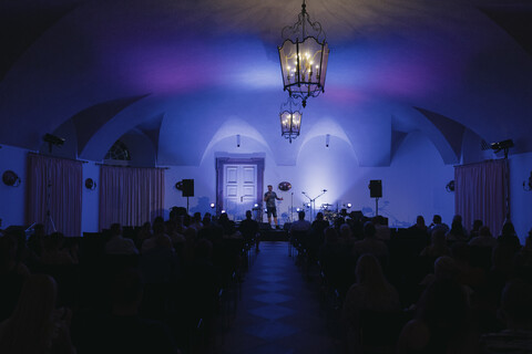 Blick auf die Bühne vom Gartensaal. Klein auf der Bühne zu sehen ist der Comedian Toby Käp. Vor ihm sitzt das Publikum.