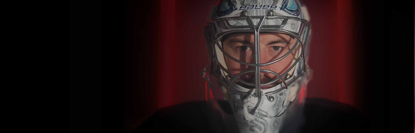 Seattle Kraken Goalie, Philipp Grubauer in his full face mask against a red background