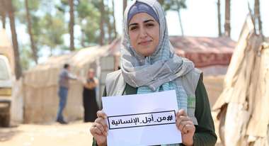 Frau in Syrien hält ein Schild mit einem Hashtag auf Arabisch