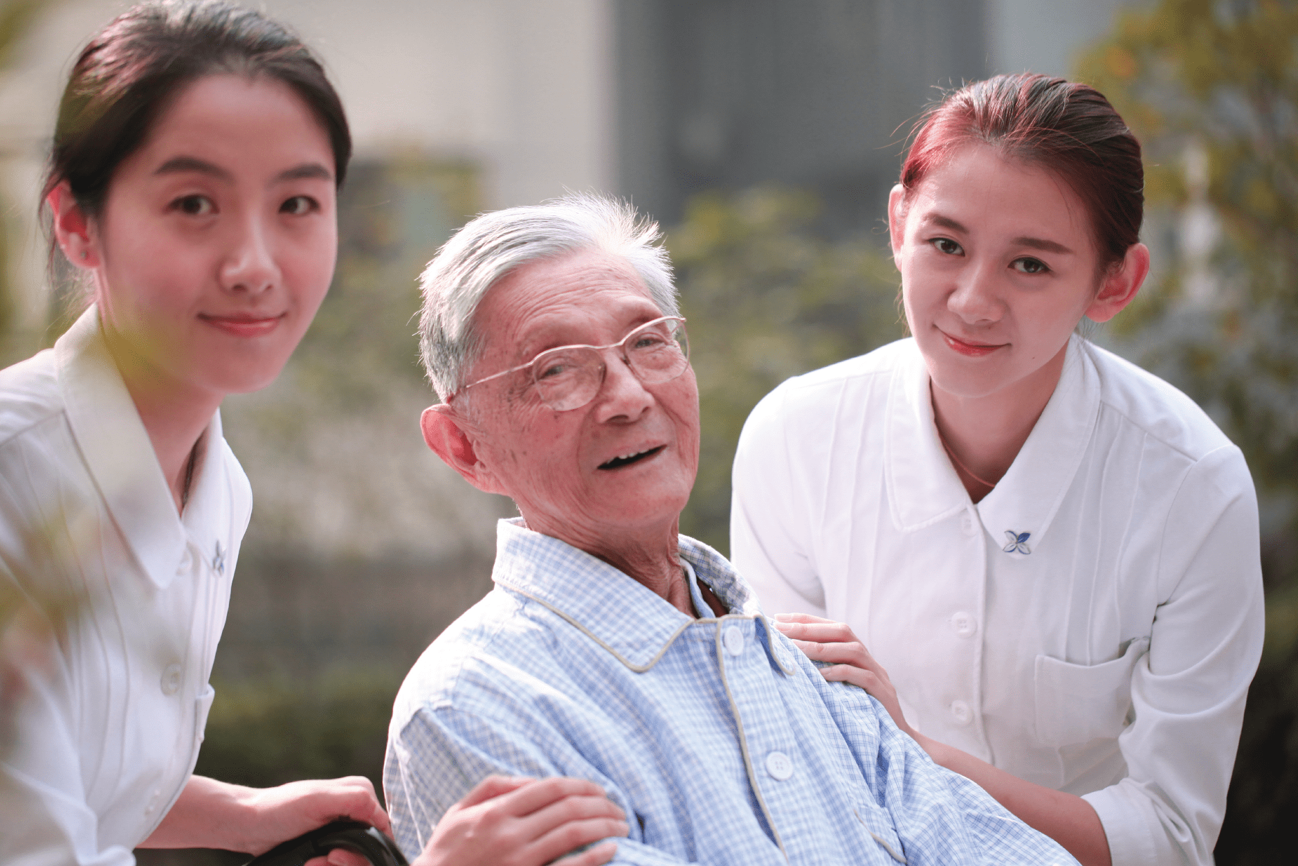 Two care professionals supporting an older man in a wheelchair explore a garden.