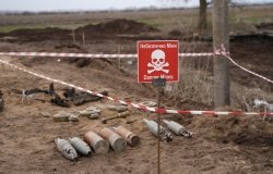 Unexploded ordinance lying in a field next to a red warning sign