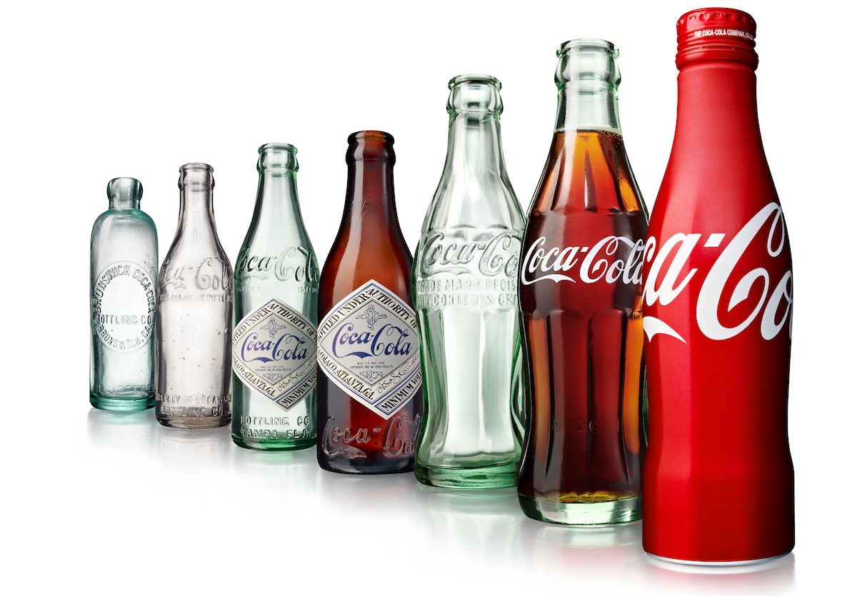 The full line up of iconic Coca-Cola bottles, starting with the 1899 bottle in the back left and ending with the aluminum bottle of 2005