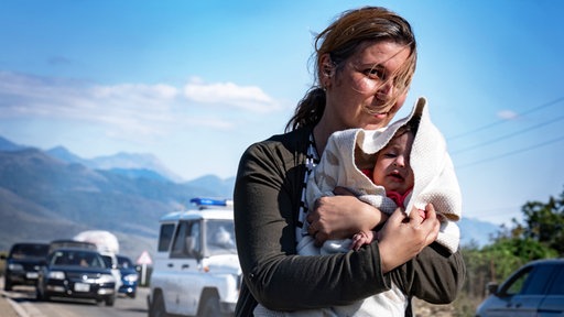 Eine Frau hält ein kleines Kind schützend in ihren Armen 