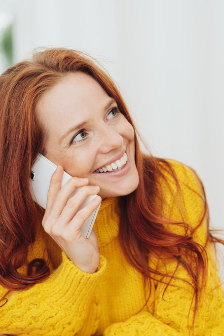 Frau mit gelbem Pullover telefoniert mit Mobiltelefon