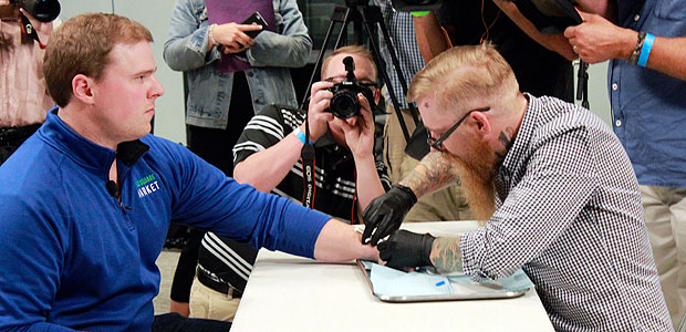 Tony Danna, left, vice president of international development at Three Square Market in River Falls, Wis., receives a microchip in his left hand at company headquarters Tuesday, Aug. 1, 2017. The company is making microchips available to its employees, allowing them to open doors, log onto their computers or buy breakroom snacks by simply waving their hand. (AP Photos/Jeff Baenen) ORG XMIT: RPJB102