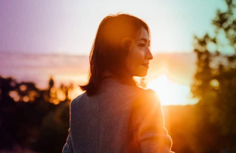 Cytalux - Woman standing outside facing the sun as it sets