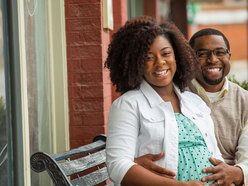 Casal heterossexual negro, ela gestante, sentado num banco sorrindo