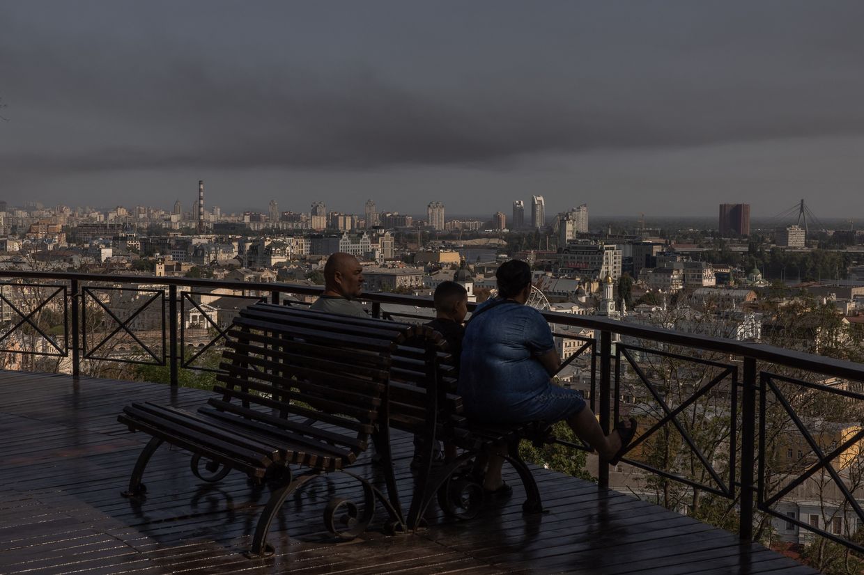 A man, a woman and a child look on as smoke rises over buildings in Kyiv, Ukraine following a Russian air attack on Aug. 26, 2024