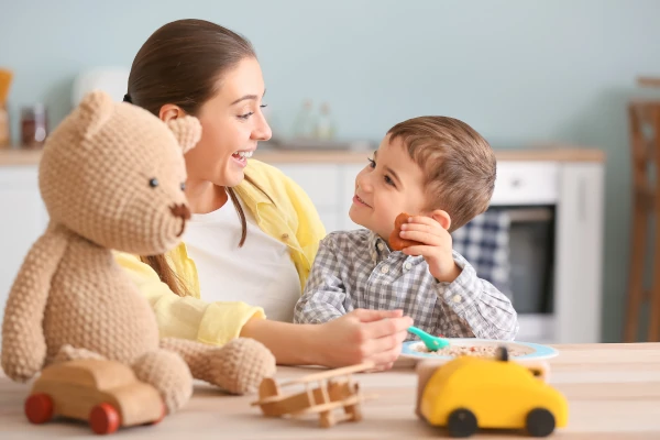 Nanny feeding cute little boy in kitchen