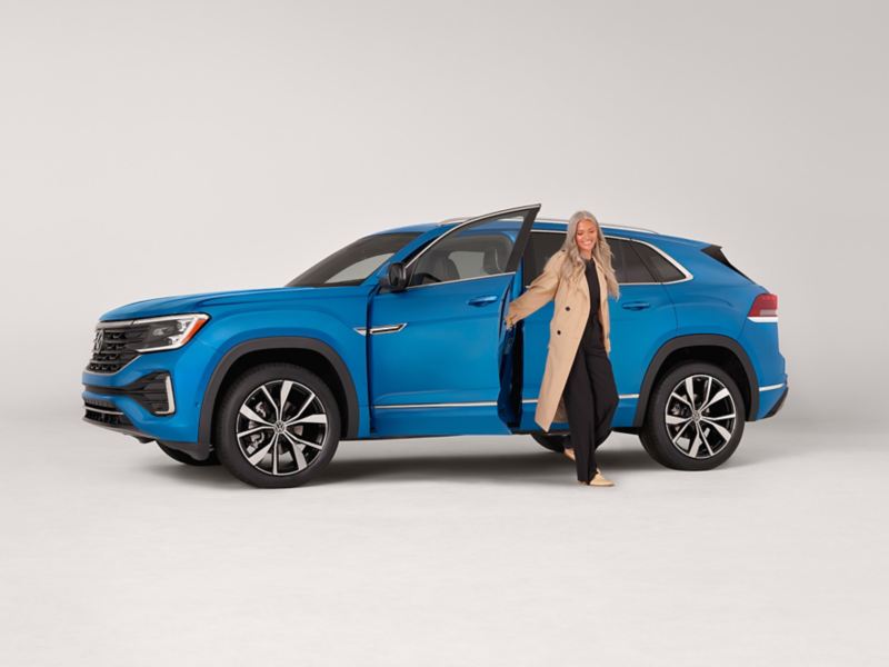 Person exiting an Atlas Cross Sport shown in Kingfisher Blue Metallic parked on a white background.