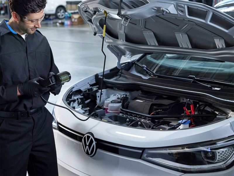 A technician stands next to an ID.4 with a diagnostic tool attached in a mechanic shop.