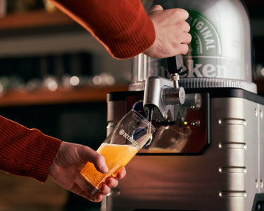 A person pours a glass of Heineken beer into a Beerwulf beer glass from a BLADE beer machine.