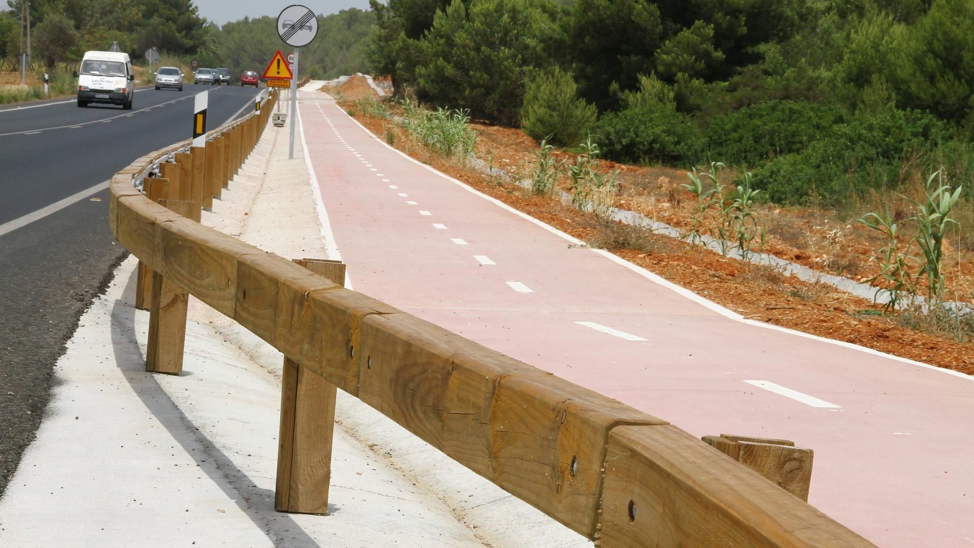 Eine Straße mit Pkws in Spanien. Straße und Radweg sind durch hölzerne Leitplanken getrennt.