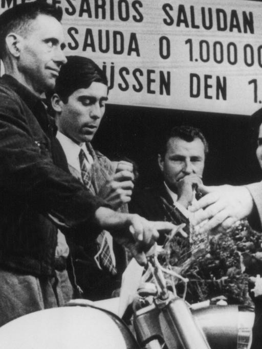 Der millionste Gastarbeiter in der Bundesrepublik, Armando Rodrigues (l.) aus Portugal, steht neben dem Moped, das er bei seiner Ankunft am 10.09.1964 im Köln-Deutzer Bahnhof geschenkt bekam.