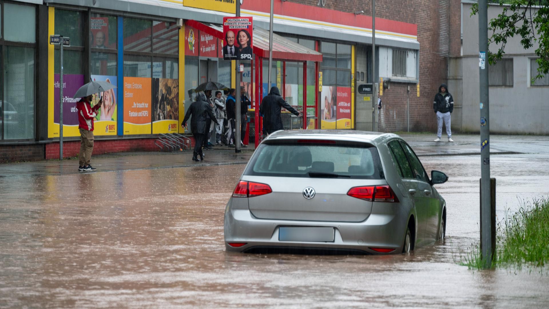 Passanten stapfen und fahren durch das Hochwasser in der Fischbachstraße in Saarbrücken. Nach starken Regenfällen steht diese teilweise unter Wasser.