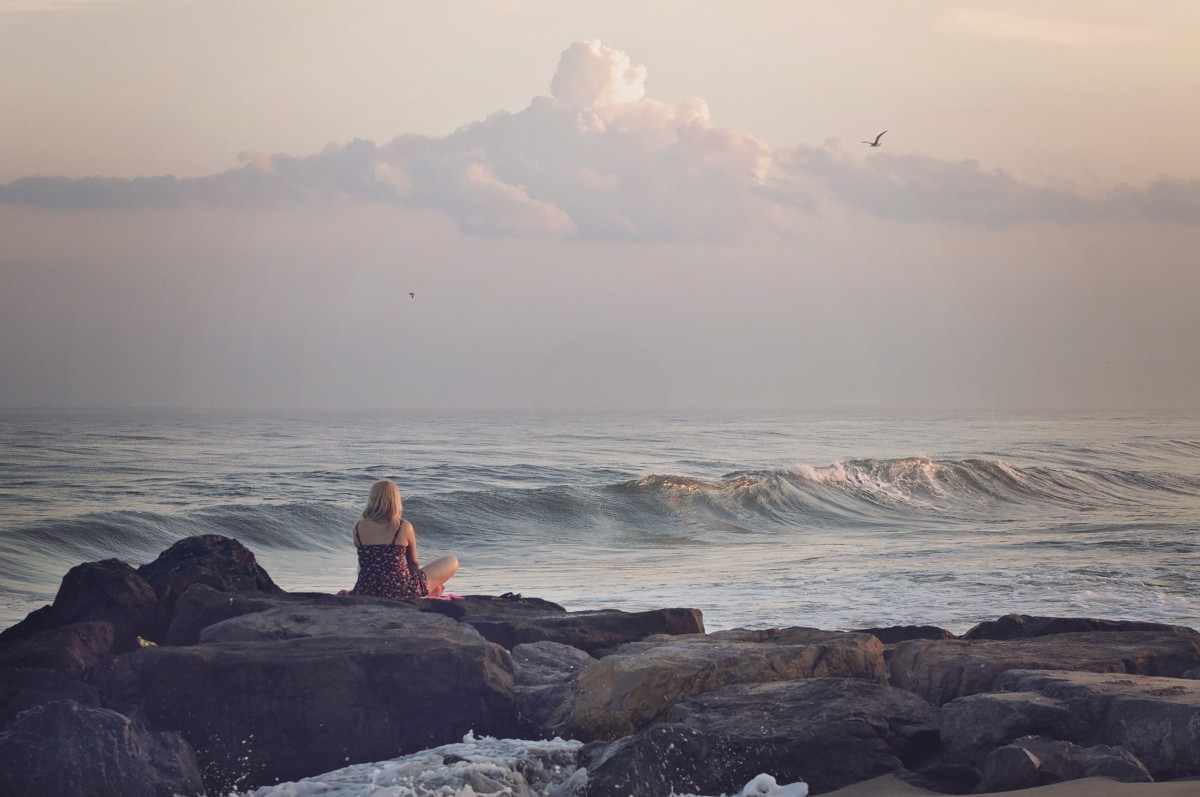 beach, sea, coast, water, nature, sand, rock, ocean, horizon, person, cloud, woman, sunrise, sunset, morning, round, shore, wave, view, dawn, vacation, cliff, seaside, dusk, female, evening, sitting, holiday, bay, terrain, body of water, rocks, stones, waves, clouds, boulders, breakwater, cape, atmospheric phenomenon, wind wave