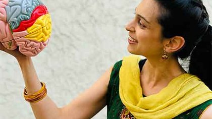 Caltech student Jessleen Kanwal holding and looking at a colorful model of a human brain