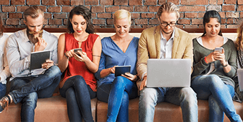 Multiple people seated on a bench reading a blog on various devices