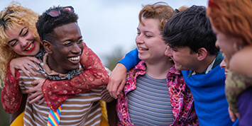 Multiracial group of teenage friends standing with and smiling at transgender teen wearing makeup.