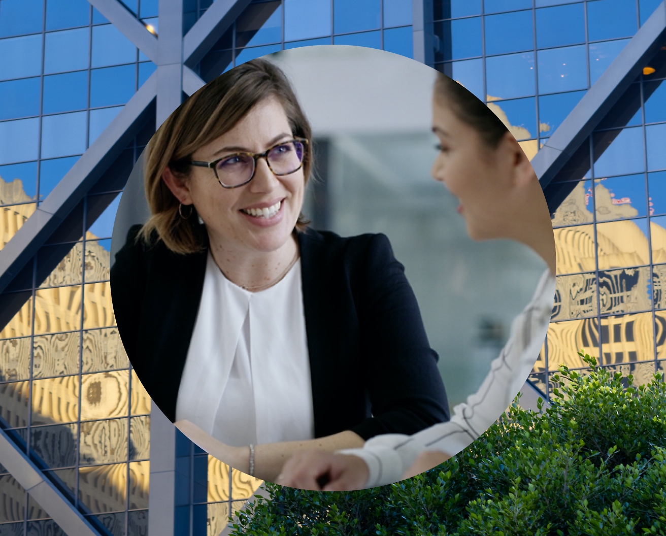 Two women discussing with background as glass building