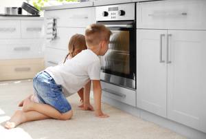 Backofen im Test: Zwei kleine Kinder hocken vor dem Backofen und sehen durch das Fenster hinein.