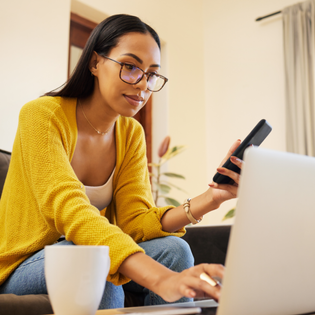 Woman holds phone while scrolling on her laptop.