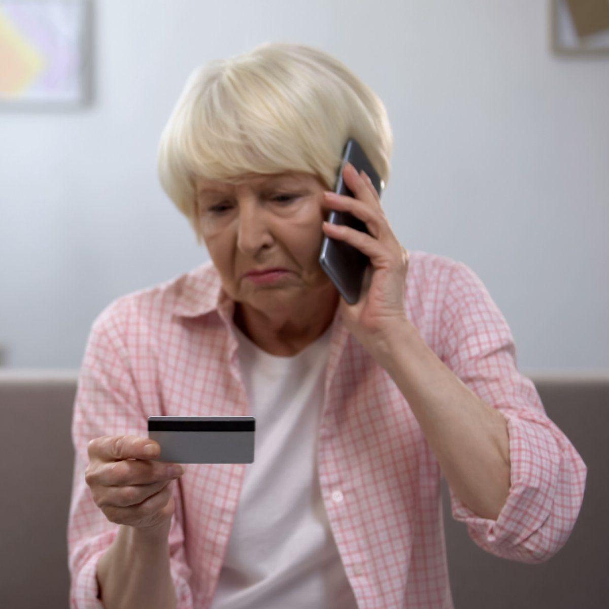 Senior lady looks upset on the phone as she looks at her credit card
