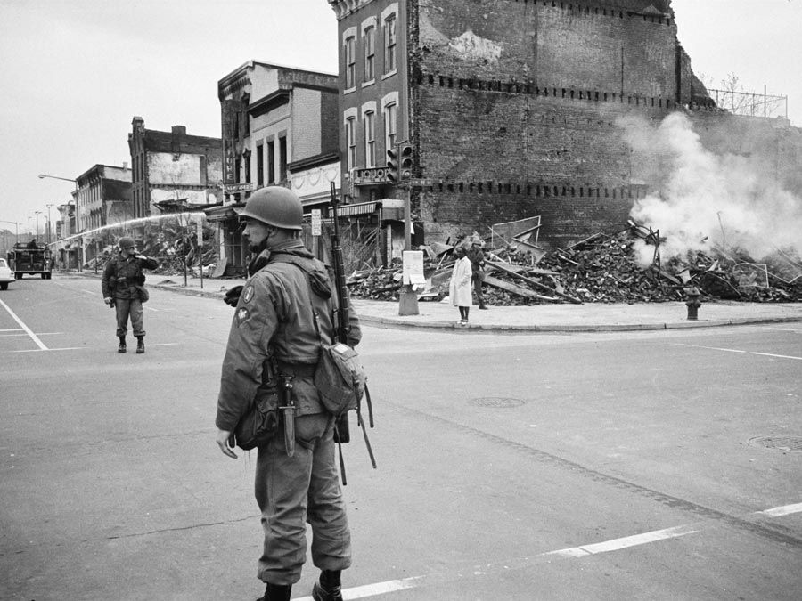 A soldier standing guard in a Washington, D.C. street with the ruins of buildings that were destroyed during the riots that followed the assassination of Martin Luther King, Jr., April 8, 1968.