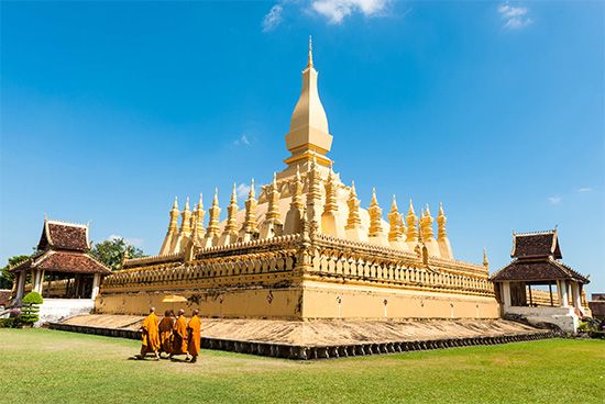 Buddhist monks walking past the Pha That Luang temple, Vientiane, Laos.