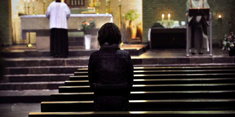 Katholieke kerkdienst, priesters en gelovige biddend in beeld