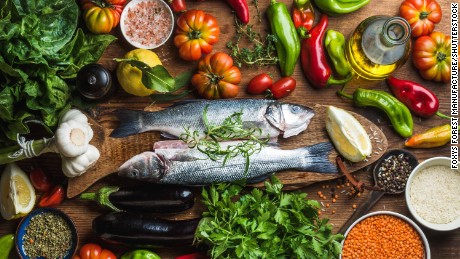 Raw uncooked seabass fish with vegetables, grains, herbs and spices on chopping board over rustic wooden background, top view; Shutterstock ID 415721434