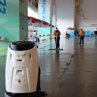 メインメディアセンターのロビーをモップがけするロボットと清掃スタッフ＝中国・北京で2022年2月8日午後5時11分、長澤凜太郎撮影